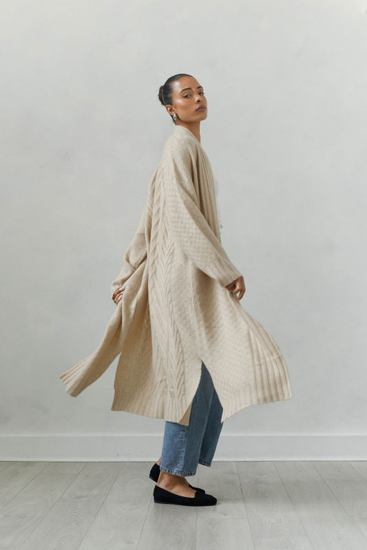 Woman wearing a long beige cardigan against a plain background