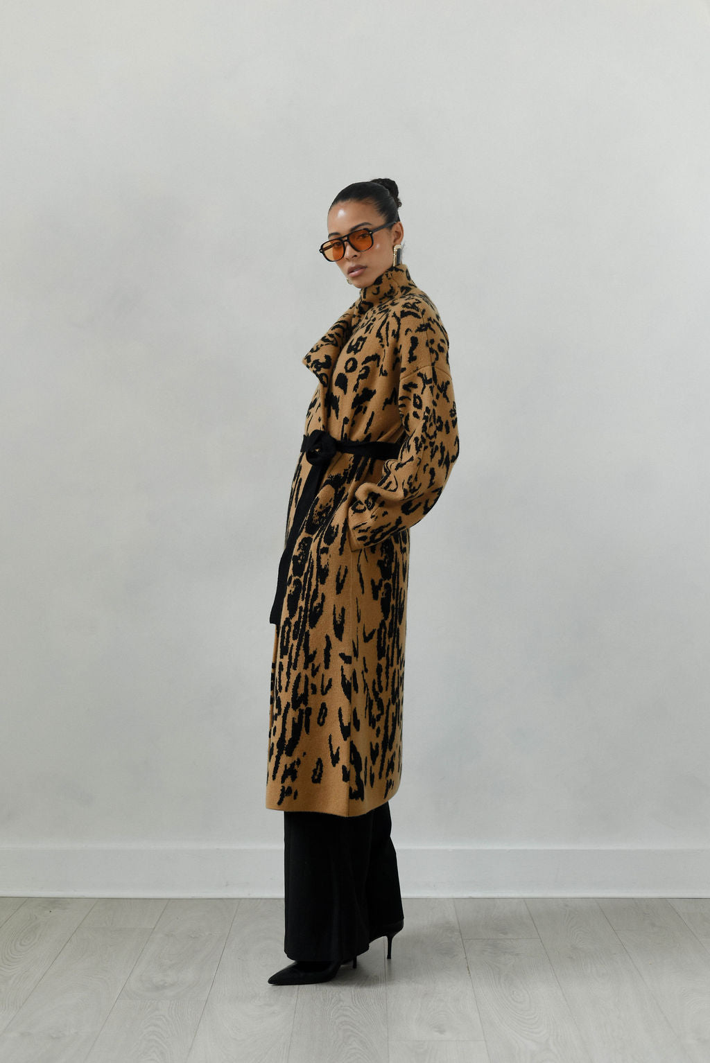 Person wearing a long leopard print coat against a plain background