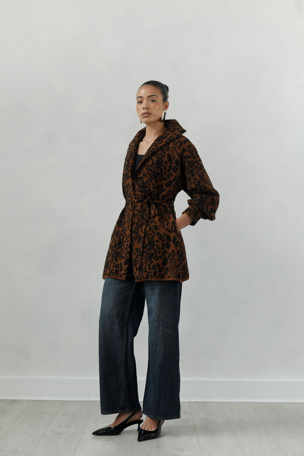 Person wearing a brown patterned coat and blue jeans against a white background