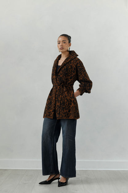 Person wearing a brown patterned coat and blue jeans against a white background