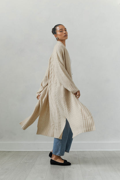 Woman wearing a long beige cardigan against a plain background