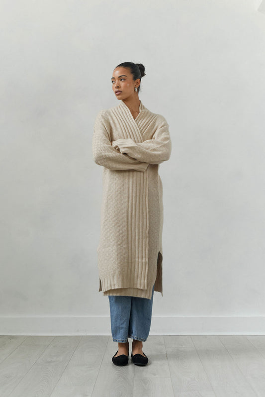 Woman wearing a beige cable knit cardigan against a white background