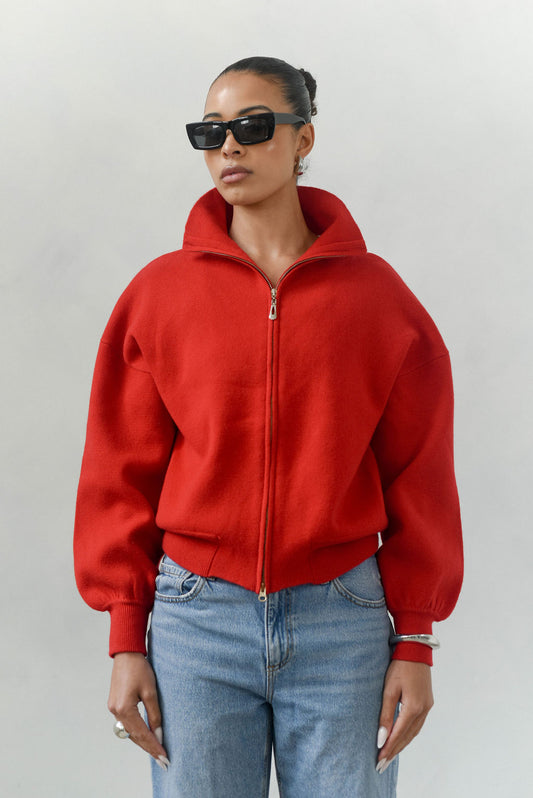 Person wearing a red jacket and blue jeans against a plain background