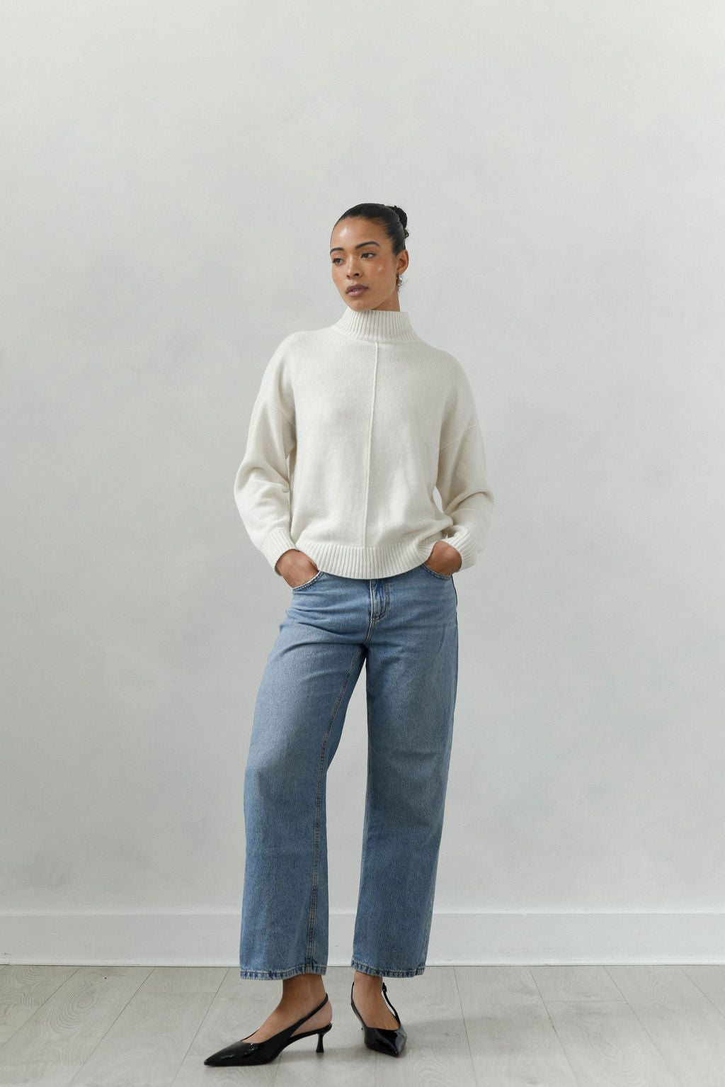 Person wearing a white sweater and light blue jeans against a plain background