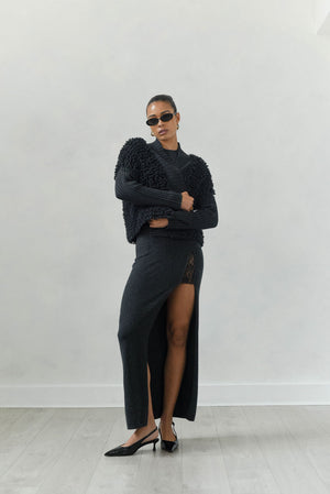 Woman wearing a black outfit with a high slit skirt against a white background