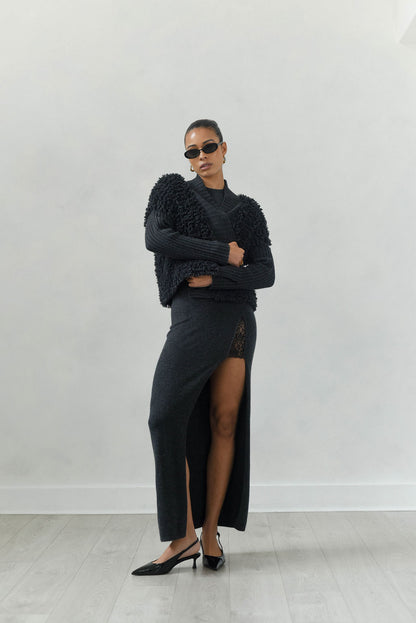 Woman wearing a black outfit with a high slit skirt against a white background