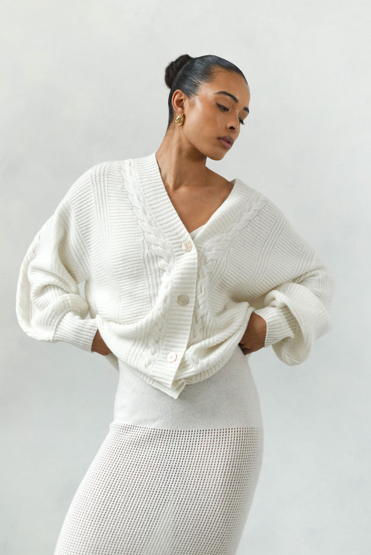 Woman wearing a white knit cardigan over a matching dress against a plain background